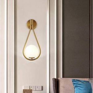 Applique murale dorée avec boule lumineuse sur un mur clair