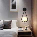 Applique murale noire avec boule lumineuse au-dessus d’une table de chevet.